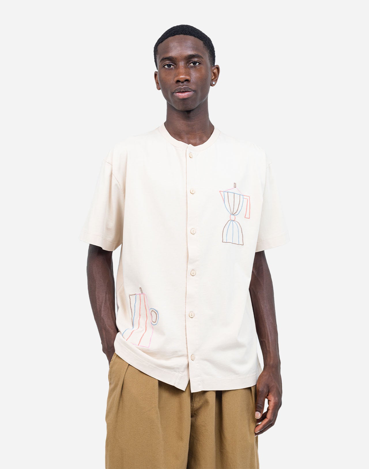 For those who mark their days with coffee breaks, this buttoned organic cotton T-shirt is made with you in mind. The fine line of artist Caìt McEniff is delicately embroidered in soft pastel tones, adding a subtle touch of color.
