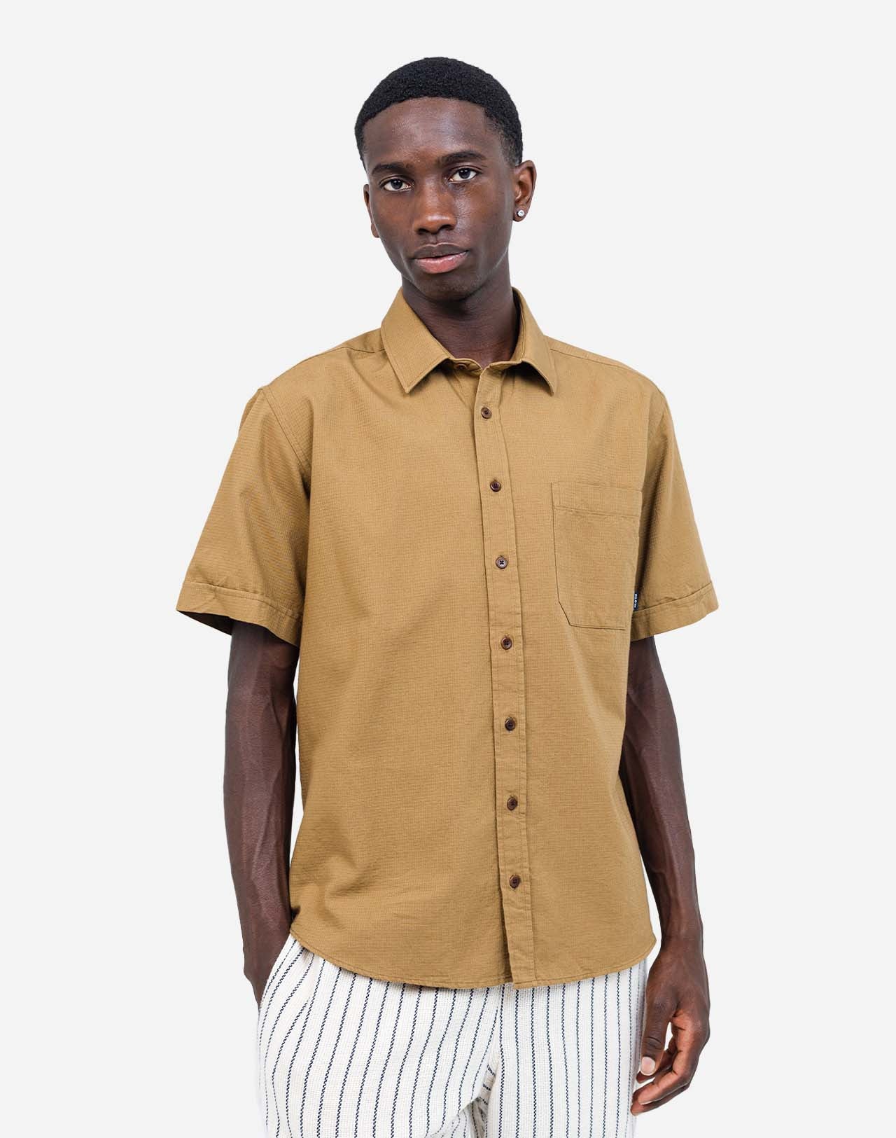 With its earth tone, this short-sleeved shirt brings a sober and natural touch to any summer wardrobe. Its loose fit creates a relaxed silhouette, making it an easy piece for daily wear. Crafted from cotton and featuring corozo buttons, the Lewis Terre shirt offers a comfortable and structured fabric.