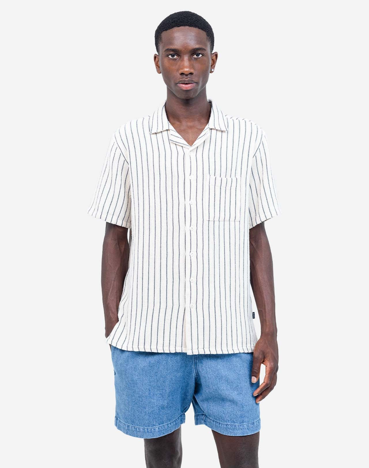 Fine vertical stripes bring a sober and summery elegance to this Hawaiian-cut short-sleeved shirt. A fluid and relaxed silhouette, ideal for sunny days and summer evenings alike. Crafted from 65% cotton and 35% recycled cotton (205g) and featuring corozo buttons, the Aloha Rivas shirt combines the perfect mix of comfort and structure.

