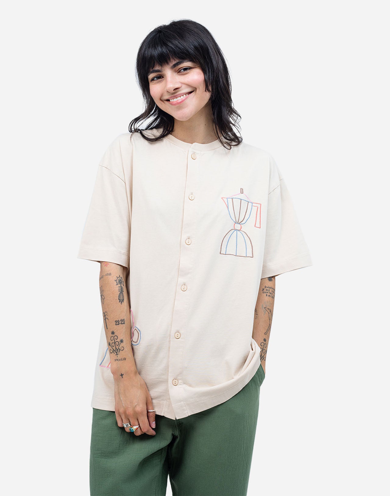 For those who mark their days with coffee breaks, this buttoned organic cotton T-shirt is made with you in mind. The fine line of artist Caìt McEniff is delicately embroidered in soft pastel tones, adding a subtle touch of color.
