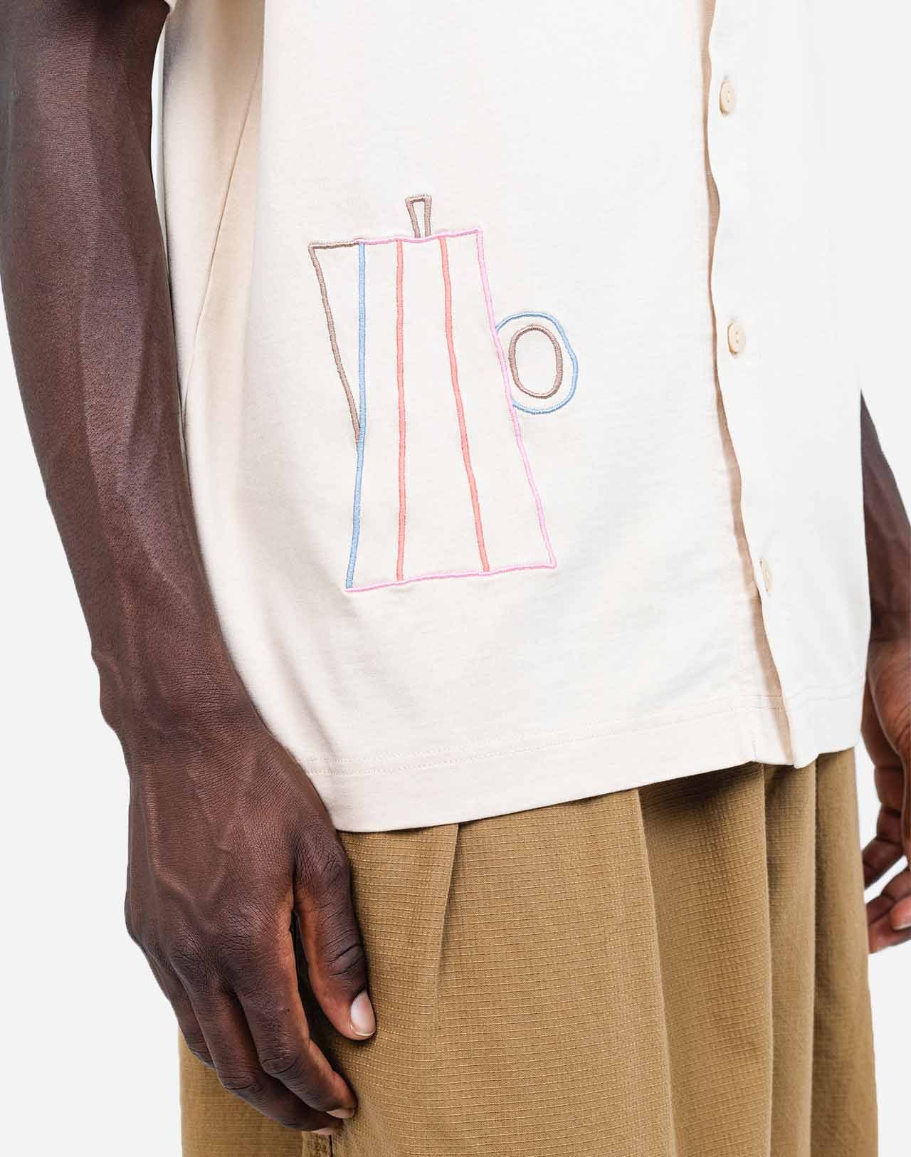 For those who mark their days with coffee breaks, this buttoned organic cotton T-shirt is made with you in mind. The fine line of artist Caìt McEniff is delicately embroidered in soft pastel tones, adding a subtle touch of color.
