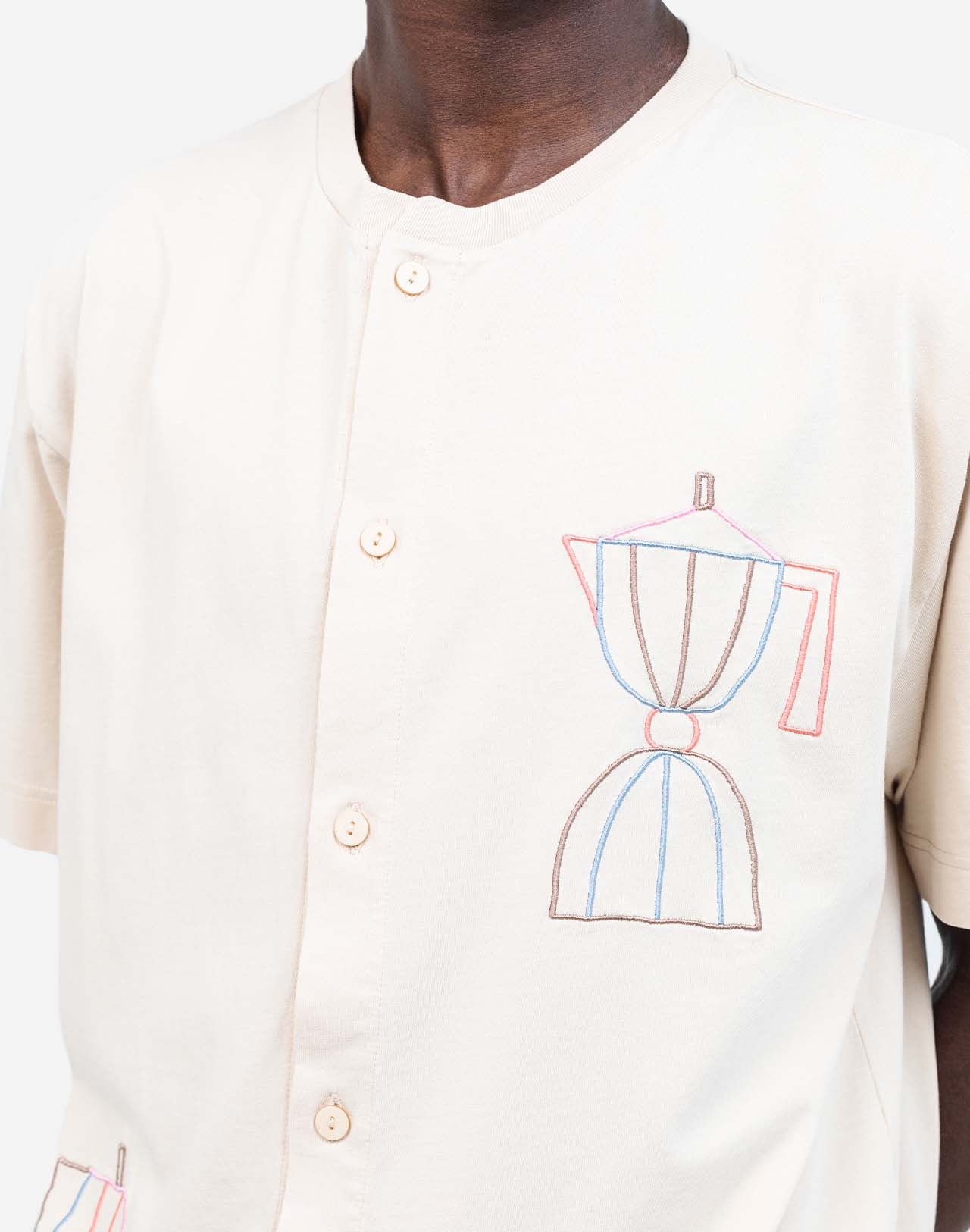 For those who mark their days with coffee breaks, this buttoned organic cotton T-shirt is made with you in mind. The fine line of artist Caìt McEniff is delicately embroidered in soft pastel tones, adding a subtle touch of color.
